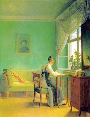 Woman doing embroidery in the light coming in through the window of a room with bright green wallpaper. A guitar lays on the couch in the background.