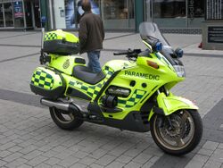 Yellow motorcycle with green battenberg livery parked without rider on a pavement.
