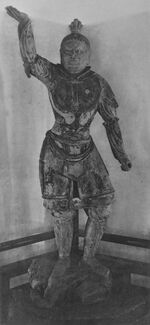 Tamonten, one of the Four Heavenly Kings in the Kaidan Hall. Portrait of a statue in front view. The right arm is raised, the hair sculpted with a top knot and the breast with armour. Narrow slit eyes and a facial expression as if frowning.