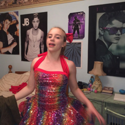 A photograph of Eilish wearing a rainbow-colored dress in front of a Justin Bieber-postered wall