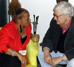 An image of a woman in a red dress speaking with a man, both sitting down.