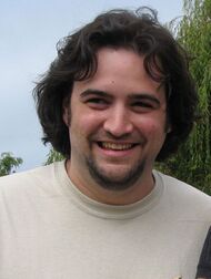 Causcasian man with medium-length dark brown hair and a beard smiles for a camera. The man is wearing a gray T-shirt with an image of evolution from a monkey to a pirate.
