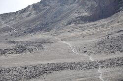 A trail runs across the curving side of a dry alpine desert of Mount Kilimanjaro.