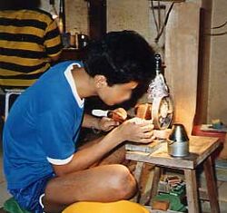 An Asian man bent over a small gemcutting machine on a low table.