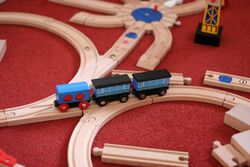 Blue toy trains on wooden interlocking tracks on a red rug