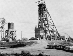 A wooden frame above the mine's shaft, an above-ground water tank, and three parked cars