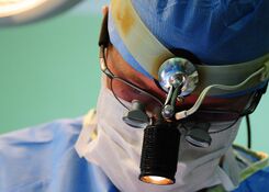 Surgeon wearing scrubs and a face mask while undergoing a surgical procedure.
