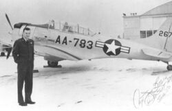 A radial piston-engined aircraft on a snowy airfield, a hangar behind and its pilot in front, with U.S. Air Force insignia and "AA-783" code below the cockpit