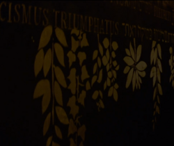 Lettering and vegetable embellishment in gold letters on a dark wall. You can partially read: "cismus triumphatus".