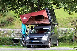 A hybrid roof tent set up on a SUV in a campsite.