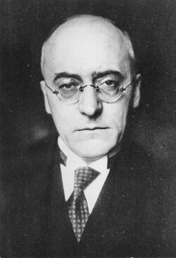 Black and white portrait of a bald, middle-aged man wearing glasses.