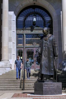 Two students walk out of Pogue Library near the statue of founder Rainey T. Wells.