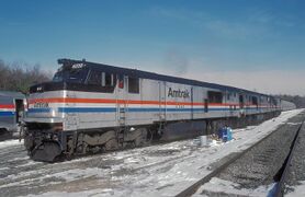 A gray diesel locomotive with a black roof. On the side are red, white, and blue stripes of equal width.