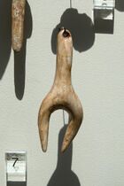 A pendant, hanging in a museum, that appears to depict a heavily stylised female figure