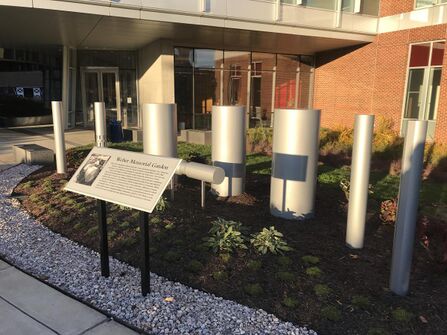 Eight large aluminum bars organized in an arch around a sign that says "Weber Memorial Garden" with a picture of Weber working on the detectors. The Garden can be found at the University of Maryland.