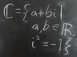 A blackboard displaying the definition: The set of complex numbers consists of all quantities a + bi such that a and b are elements of the real numbers, and i squared equals negative one. Symbolically, ℂ = {a + bi ∣ a, b ∈ ℝ, i² = −1}.