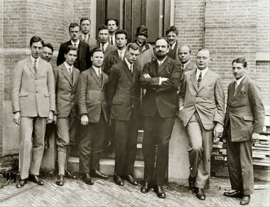 Fifteen men in suits, and one woman, pose for a group photograph