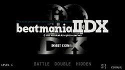 Two gears imprinted with "dj" and "II" are placed above the widened letters "DX" to form a silver metallic logo over a black background. It is partially covered by the slab-serif Beatmania IIDX logo, accompanied by Konami's brief copyright information and the dark blue text "The ultimate system beatmania deluxe version." "Insert Coins(s)" appears slightly off the center of the title screen, and "Level 4", "Battle Double Hidden", and "0/1 0/2 coin(s)" are seen at its bottom side.