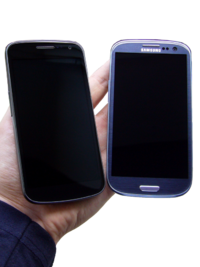 Photo of two phones turned off held next to each other with warm yellow ambience lightning. The phones are rested on a person's hand.