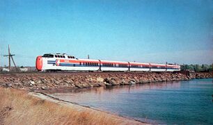 A white passenger trainset with red and blue horizontal stripes on the side and red noses on both ends