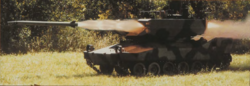 A woodland camouflaged AGS LOSAT system fires a missile. A backblast emanates from the rear of the turret. The turret appears more boxy than the original AGS turret.