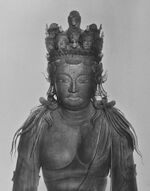 Frontal view of the head of a sculpture of a deity. A number of small heads and small statues are placed on top of the head.