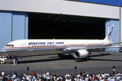 Side quarter view of twin-engine jetliner in front of hangar, with surrounding crowds