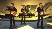 A virtual music set, composed of a small, round elevated stage and a further offset for the drum set, with several yellow-tinted arrow-like shapes mounted behind and in front of it, the arrows directed to the stage. The virtual Beatles are performing on this set.