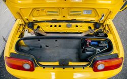 A yellow car with the trunk open, revealing a relatively small storage area