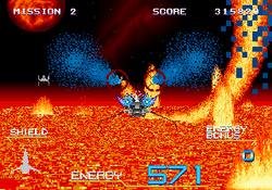 The player ship flies over a fiery planet surface. The GUI shows the shield, energy, energy bonus, score, and mission.