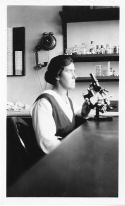 Photograph of Kirkbride Farr at a desk with microscope, lab equipment on shelves