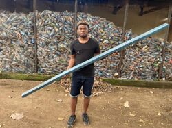 A man holding a board made from plastic in front of bags of PET bottles.