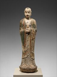 Colored limestone sculpture of monk holding an unidentified object