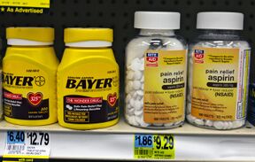 Four plastic bottles of medication on another drugstore shelf above their price tags. The two on the left are yellow with the word "Bayer" prominent in black type; above small type describes the product as "genuine aspirin". On the left are two clear plastic bottles with the Rite Aid drugstore chain logo on their yellow labels, which describe the product as "pain relief aspirin".