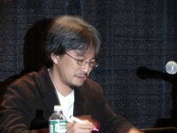 A photo of a bespectacled Eiji Aonuma near a microphone