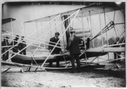 Wilbur Wright examining canoe attachment to aeroplane before 1st flight over water (3b25549u).jpg