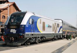 A diesel locomotive with navy blue curved shapes on the front and rear with yellow accents, a black cab area, and Amtrak California logos on the front and sides