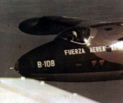 A close-up of a jet in flight, the pilot is wearing a white helmet. On the nose of the plane are the Spanish words "Fuerza Aerea Argentina" and the designation code "B-108".