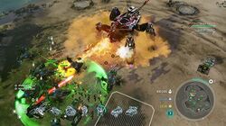 Units battle on a plain. In the bottom left are an assortment of human tanks and helicopters—angular, accented with green. The human units are surrounded by a green circular aura. In the center is a quadrupedal, metallic Covenant vehicle shooting a yellow energy beam at human units.