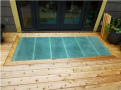 Pine decking with a panel of fiberglass showing a fine grid set in a mitered pine frame. The fiberglass is slightly blue-green, and sits squarely in front of the glass doors to the house.