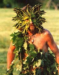 Photograph of a man wearing a green mask and leaves over his body