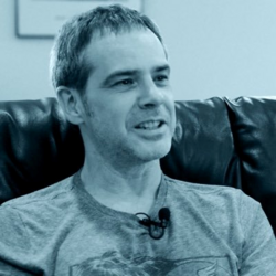 A blue duotone headshot photo of a white man with a short haircut in T-shirt.