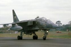 Jet aircraft in mostly green camouflage scheme taxiing.