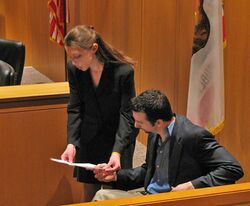 A woman and a man reading a document in a courtroom