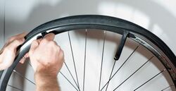 A bicycle wheel who's tire is currently being removed. One hand is pulling on the tire, while another is using a tire lever to remove it. Another lever is hooked onto a spoke.