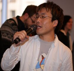 A man speaks through a microphone, talking to the audience.