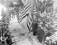Example 2: Labor strikers of the Industrial Workers of the World holding American flags, held back by a militia bearing rifles and bayonets.