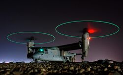 Ground crew refuel an MV-22 before a mission in central Iraq at night. The rotors are turning and the tips are green, forming green circles.
