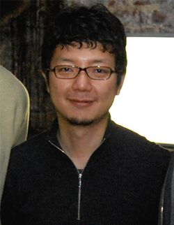 A portrait shot of a middle-aged Asian man with short, messy black hair, glasses and a zip-up sweatshirt