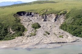 The green landscape is interrupted by a huge muddy scar where the ground has subsided.